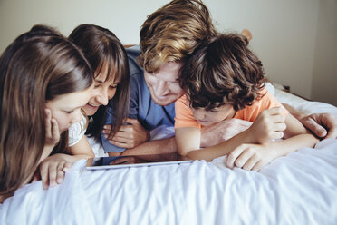 Kinder und ihre Eltern schauen auf ein Tablet auf dem Bett - MFF03728