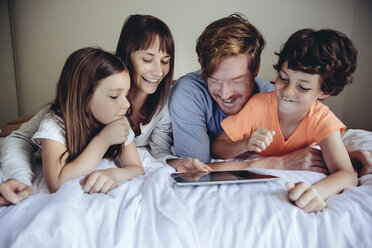 Kinder und ihre Eltern schauen auf ein Tablet auf dem Bett - MFF03729