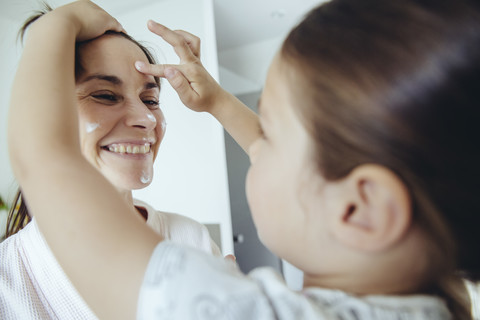 Tochter trägt Gesichtscreme auf das Gesicht der Mutter auf, lizenzfreies Stockfoto