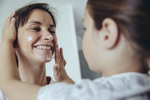 Tochter trägt Gesichtscreme auf das Gesicht der Mutter auf, lizenzfreies Stockfoto