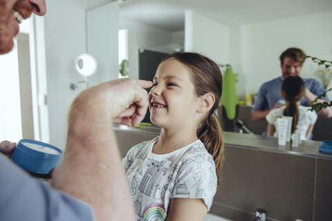 Vater trägt Gesichtscreme auf das Gesicht seiner Tochter auf, lizenzfreies Stockfoto