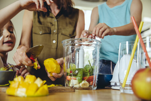 Mother and children putting fruit into a smoothie blender - MFF03752