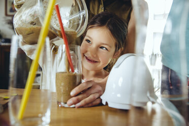 Girl pouring smoothie into glass with mother’s help - MFF03758