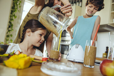 Mutter mit zwei Kindern gießt einen Smoothie in Gläser - MFF03759