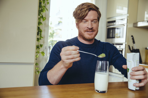 Mann gibt gesunde grüne Substanz in ein Glas Milch, lizenzfreies Stockfoto