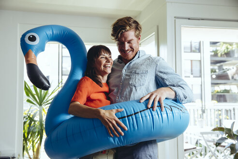 Happy couple holding an inflatable flamingo at home - MFF03781