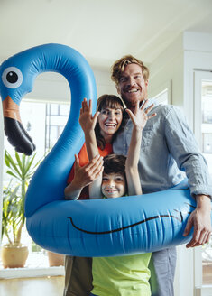 Happy parents with son holding an inflatable flamingo at home - MFF03782