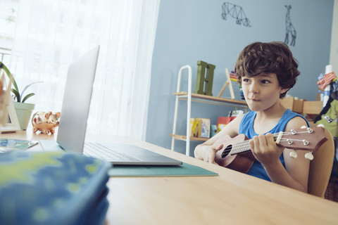 Boy using laptop to play a song on an ukulele stock photo