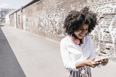 Glückliche junge Frau, die im Freien auf ihr Handy schaut - KNSF02249