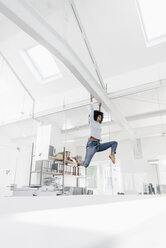 Excited young woman hanging on beam in office - KNSF02261