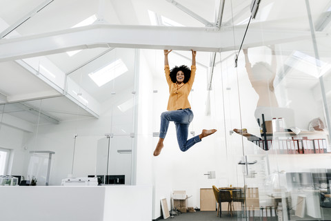 Junge Frau hängt an einem Balken im Büro, lizenzfreies Stockfoto