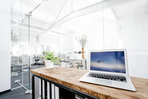 Laptop on wooden table in office - KNSF02318