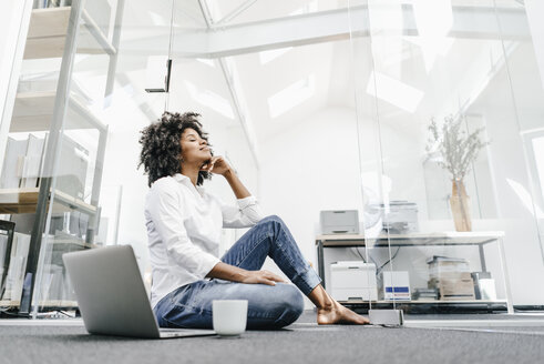 Young woman with closed eyes sitting on floor in office with laptop - KNSF02328