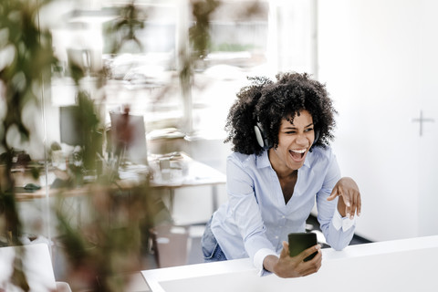 Happy young woman listening to music in office stock photo