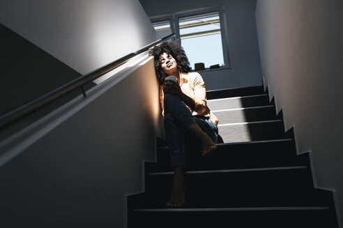 Young woman sitting on staircase in sunlight - KNSF02352