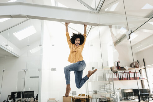 Happy young woman hanging on beam in office - KNSF02354