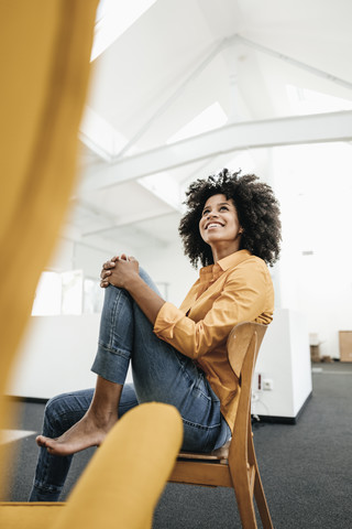 Smiling young woman sitting on chair in office looking up stock photo