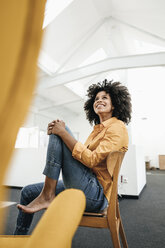 Lächelnde junge Frau sitzt auf einem Stuhl im Büro und schaut nach oben - KNSF02356