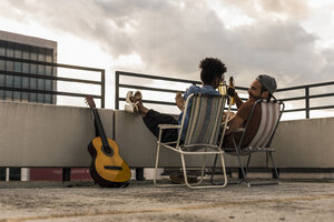 Young couple with beer and guitar sitting on rooftop - UUF11464