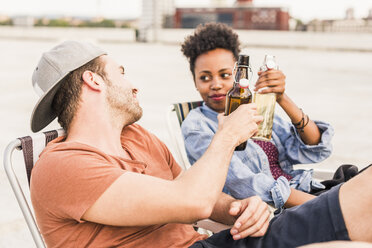 Young couple clinking beer bottles on rooftop - UUF11466