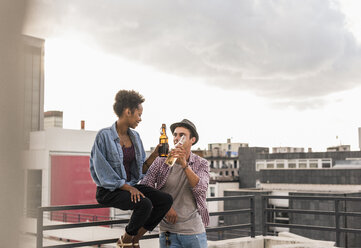 Young couple clinking beer bottles on rooftop - UUF11470