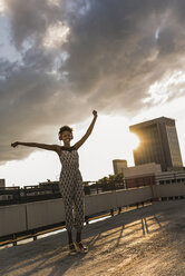 Young woman with headphones dancing on rooftop - UUF11485