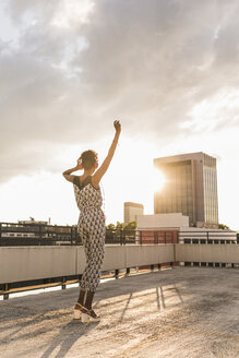 Young woman with headphones dancing on rooftop - UUF11487