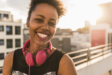 Portrait of happy young woman with headphones on rooftop - UUF11491