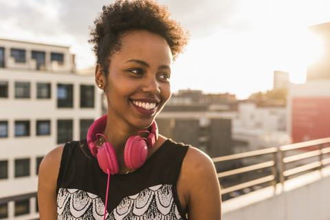 Portrait of happy young woman with headphones on rooftop stock photo