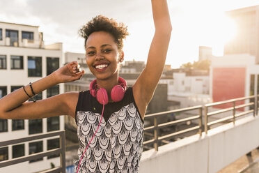 Portrait of happy young woman with headphones on rooftop - UUF11493