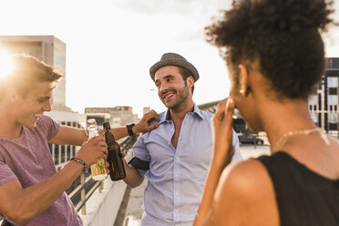 Friends clinking beer bottles on a rooftop party - UUF11502