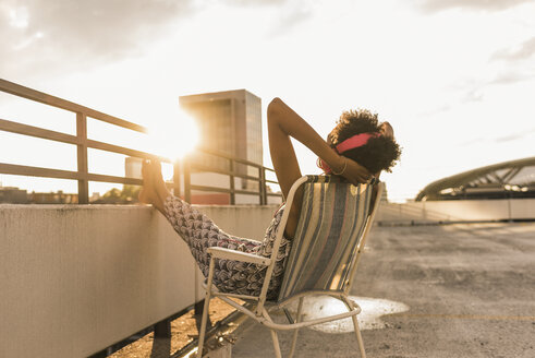 Junge Frau mit Kopfhörern auf dem Dach sitzend - UUF11504