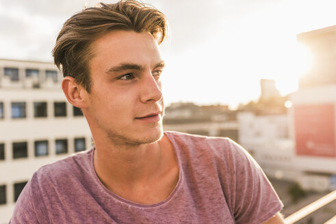 Porträt eines jungen Mannes auf einer Dachterrasse bei Sonnenuntergang - UUF11506