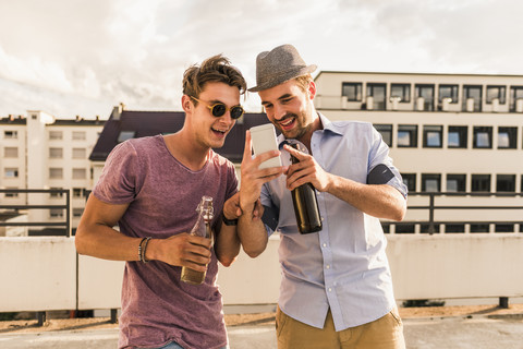 Two friends with beer bottles and cell phone on rooftop stock photo