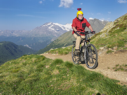 Italien Lombardei, Passo di Val Viola, Mann fährt E-Bike in den Bergen mit Action-Cam auf seinem Helm - LAF01858