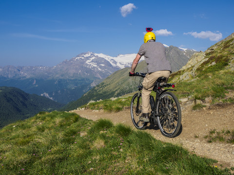 Italien Lombardei, Passo di Val Viola, Mann fährt E-Bike in den Bergen mit Action-Cam auf seinem Helm, lizenzfreies Stockfoto