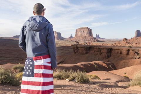 USA, Utah, Rückenansicht eines jungen Mannes mit amerikanischer Flagge im Monument Valley, lizenzfreies Stockfoto