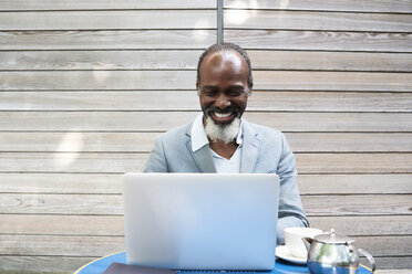 Porträt eines lachenden bärtigen Mannes mit Laptop - IGGF00091