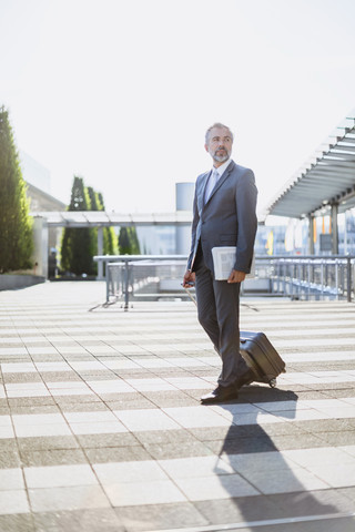 Businessman pulling rolling suitcase outdoors stock photo