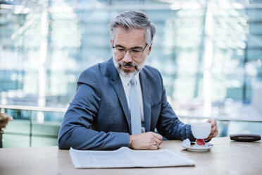 Businessman reading newspaper and drinking coffee - DIGF02624