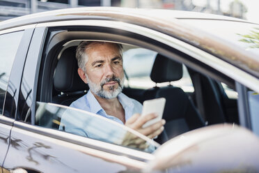 Geschäftsmann schaut im Auto auf sein Handy - DIGF02670