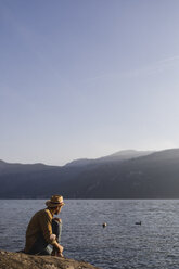 Italy, Lierna, man sitting at lakeshore enjoying sunset - MRAF00220