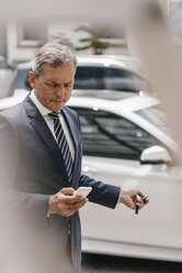Geschäftsmann, der eine Nachricht abruft, während er einen Autoschlüssel mit Fernbedienung benutzt - KNSF02392