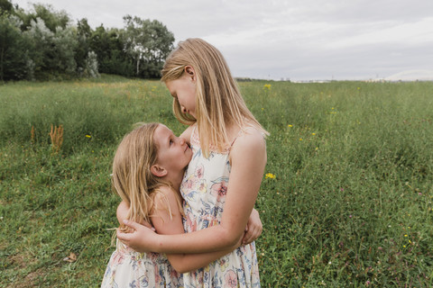Zwei kleine Schwestern umarmen sich auf einer Wiese, lizenzfreies Stockfoto