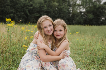 Zwei kleine Schwestern umarmen sich auf einer Wiese - NMSF00150