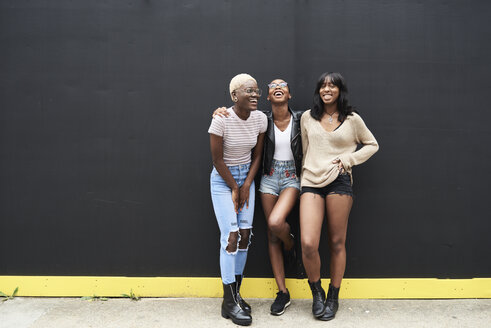 Three friends standing against black background having fun - IGGF00103