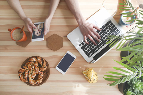 Young couple having coffee and chocolate braids using laptop and smartphone, top view stock photo