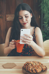 Freckled young woman with coffee mug using smartphone - RTBF00998