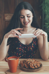 Freckled young woman taking picture of coffee and chocolate braids with smartphone - RTBF00999