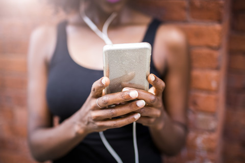 Frau hält Handy an Ziegelmauer, lizenzfreies Stockfoto